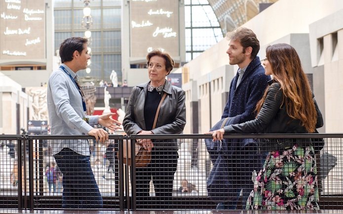 Guide with tourists inside Orsay Museum, France, discussing art exhibits.