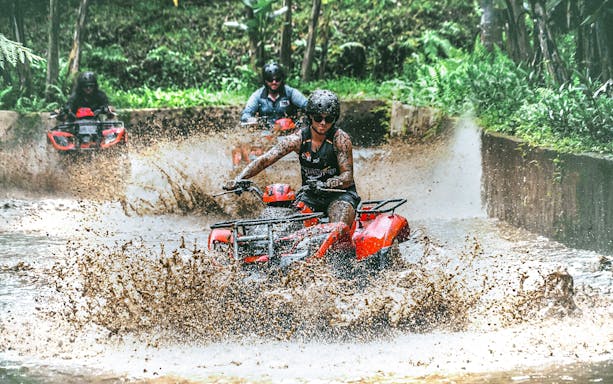 ATV riders splashing through mud in Ubud jungle adventure.