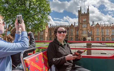 Hop-on hop-off bus near Queen's University Belfast with tourists taking photos.