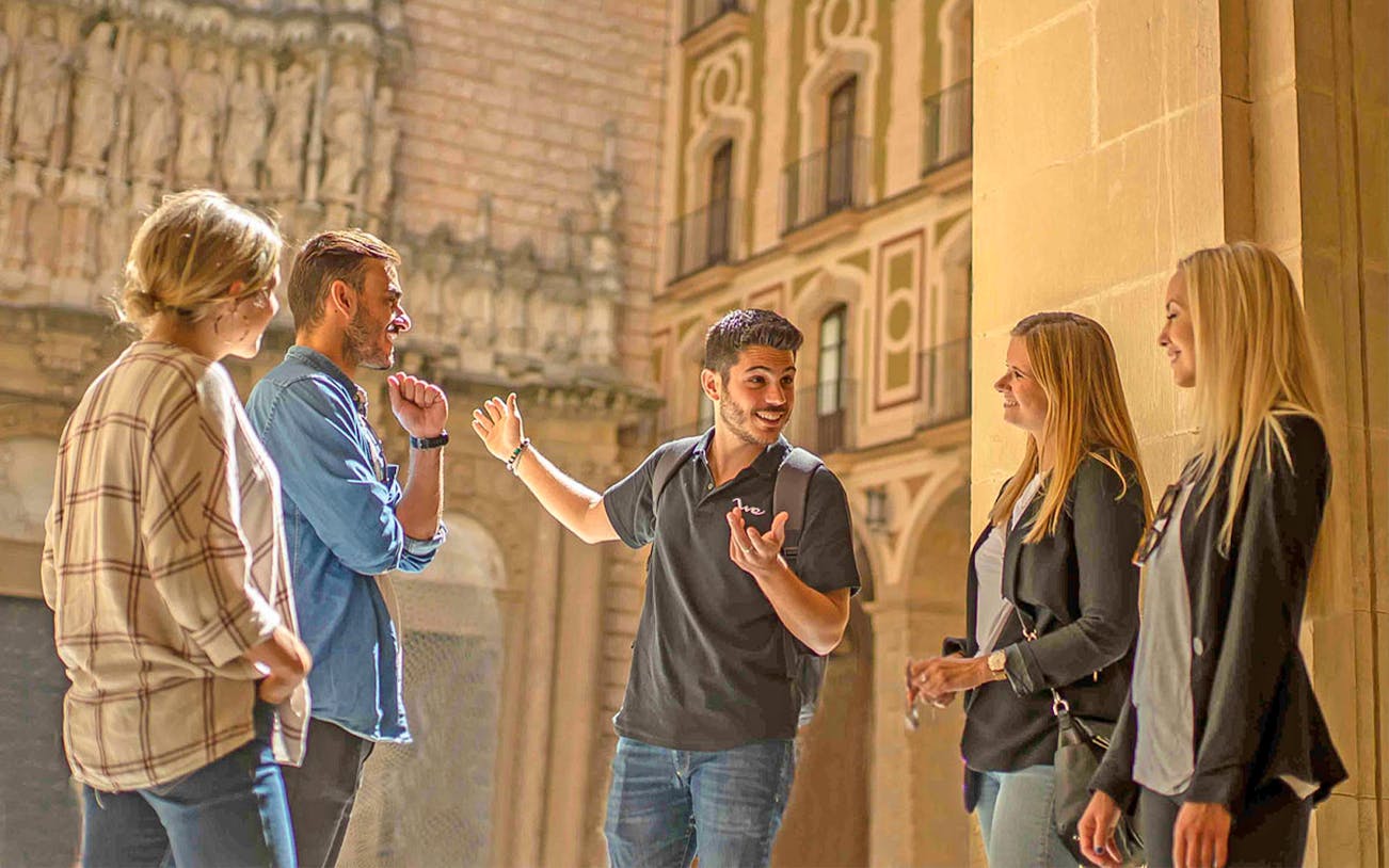 Guide explaining Montserrat Monastery history to visitors in courtyard.