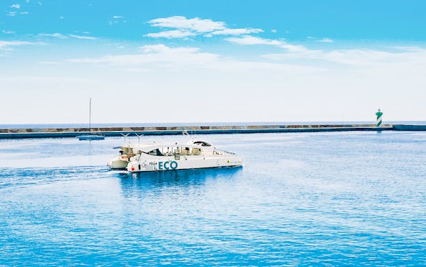 Catamaran sailing near Barcelona harbor with a distant lighthouse.