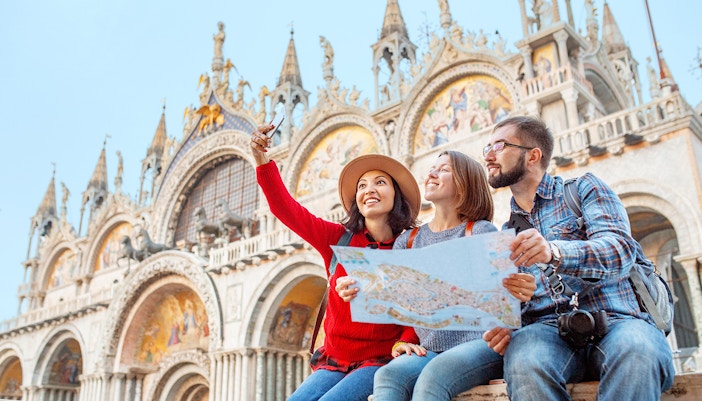 Group of happy friends travelers with map on San Marco Square in Venice.