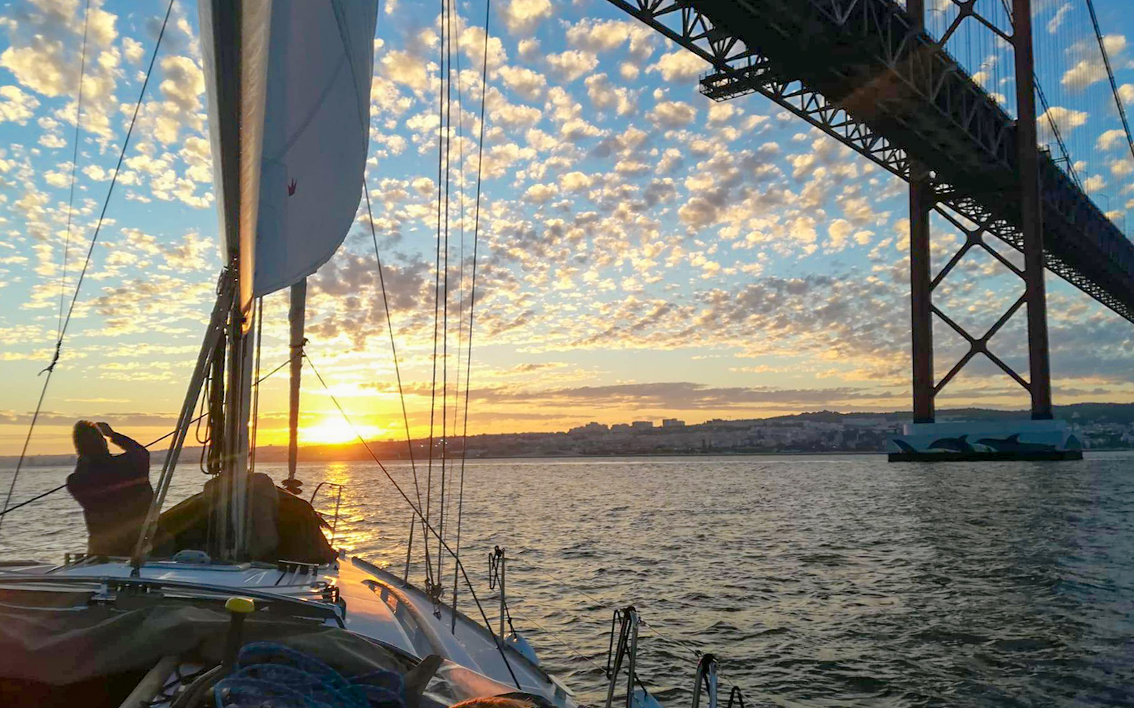 Tourist on a private boat viewing Lisbon at sunset near the 25 de Abril Bridge.