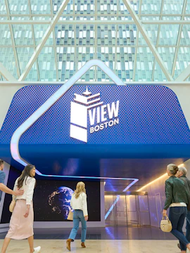 Visitors entering View Boston with illuminated signage and glass building backdrop.