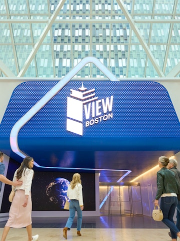 Visitors entering View Boston with illuminated signage and glass building backdrop.