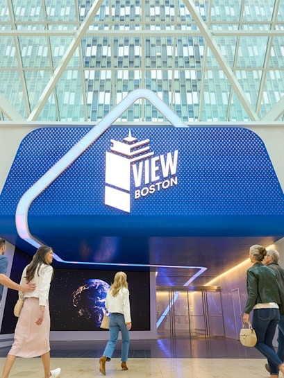 Visitors entering View Boston with illuminated signage and glass building backdrop.
