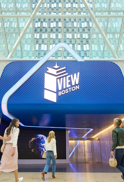 Visitors entering View Boston with illuminated signage and glass building backdrop.