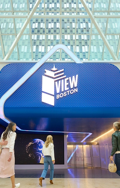 Visitors entering View Boston with illuminated signage and glass building backdrop.