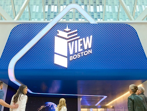 Visitors entering View Boston with illuminated signage and glass building backdrop.