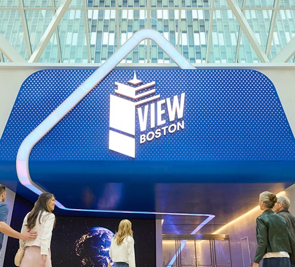 Visitors entering View Boston with illuminated signage and glass building backdrop.