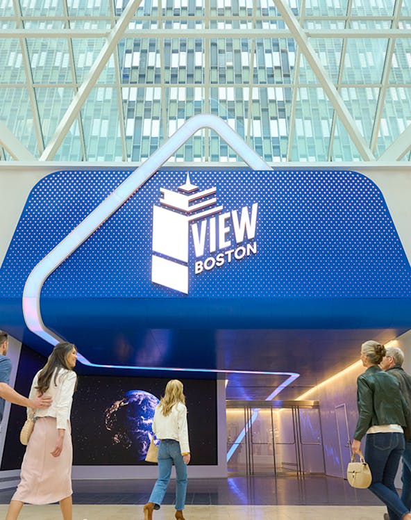 Visitors entering View Boston with illuminated signage and glass building backdrop.