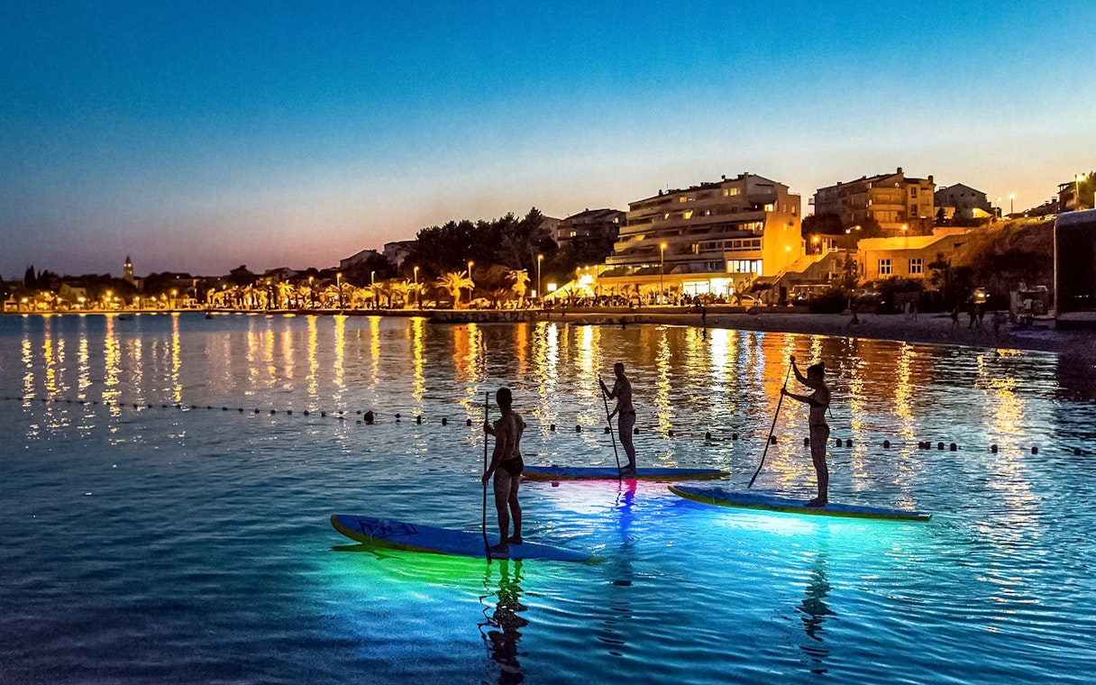 Paddleboarders on illuminated boards during SUP Glow Tour in Split at sunset.