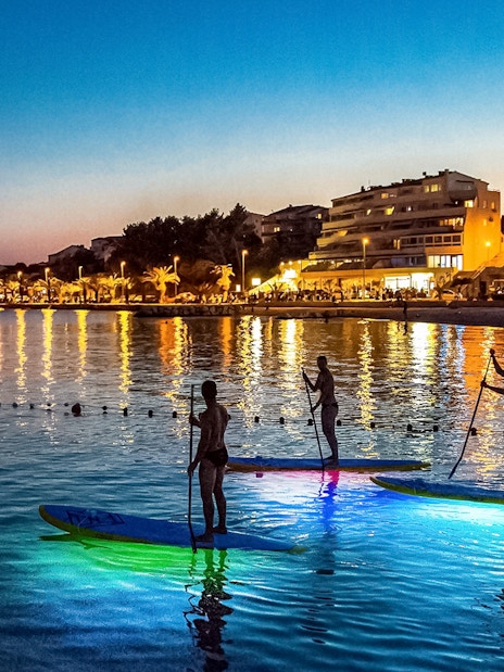Paddleboarders on illuminated boards during SUP Glow Tour in Split at sunset.