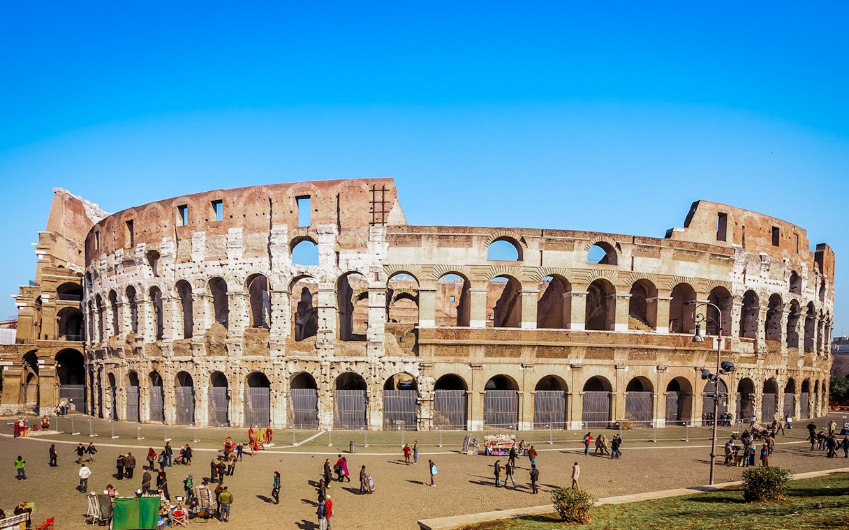 Colosseum in Rome with tourists exploring the exterior on a guided tour.