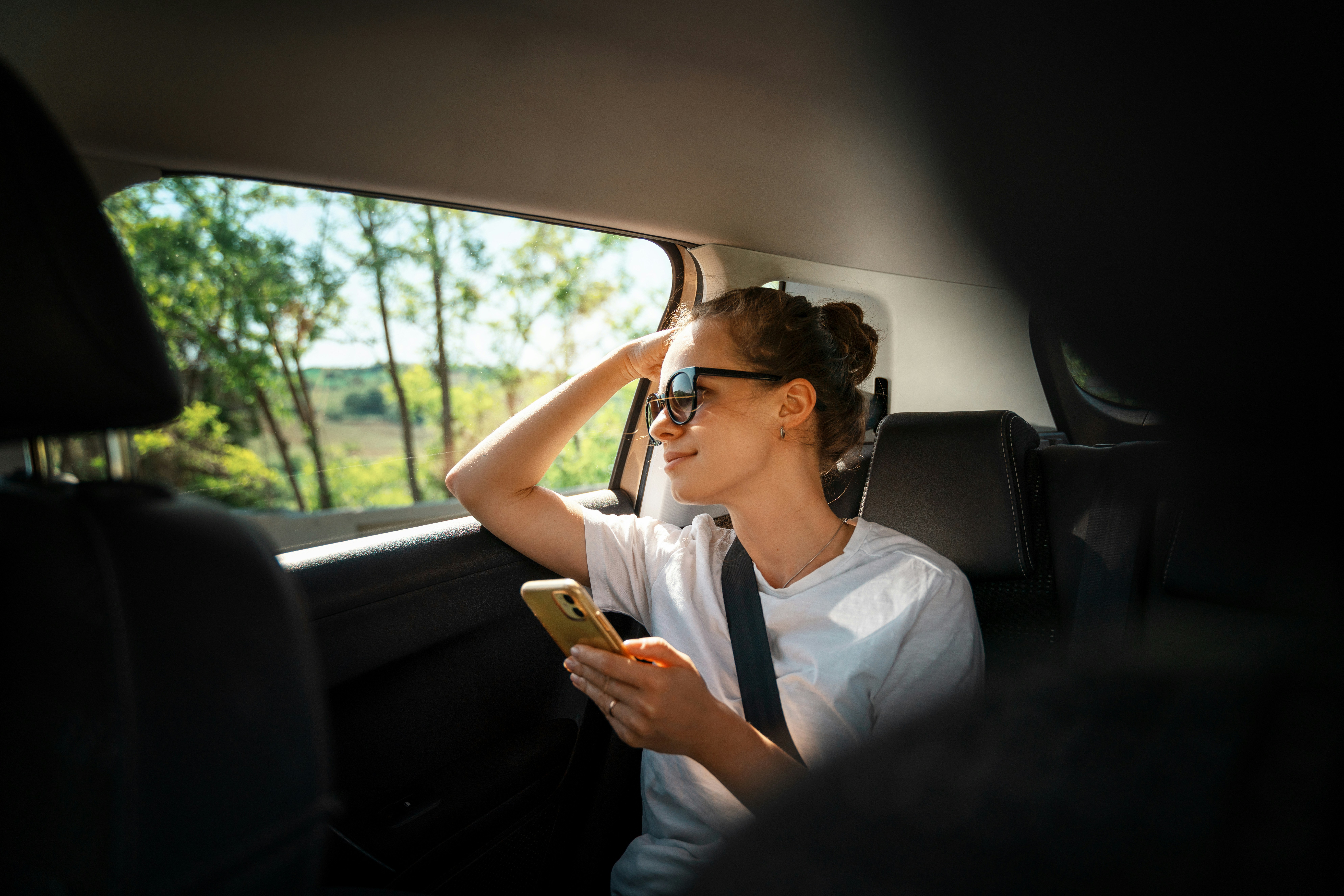 Young woman using smartphone in back seat of car, seatbelt fastened.