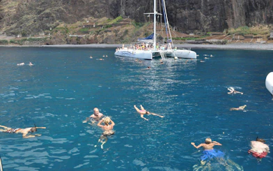 Catamaran with tourists swimming in the ocean near Funchal cliffs.