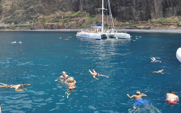 Catamaran with tourists swimming in the ocean near Funchal cliffs.