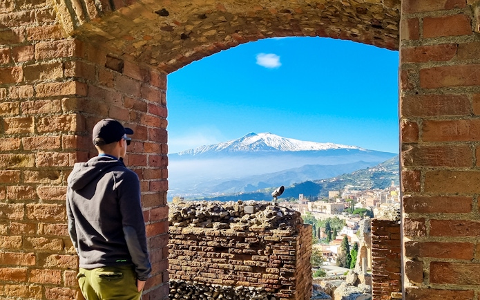 Person viewing Mount Etna through Taormina Ancient Theatre archway, Sicily.
