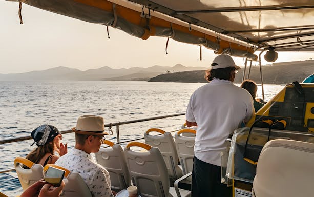 Tourists on a speedboat enjoying a sunset cruise with distant coastal views.