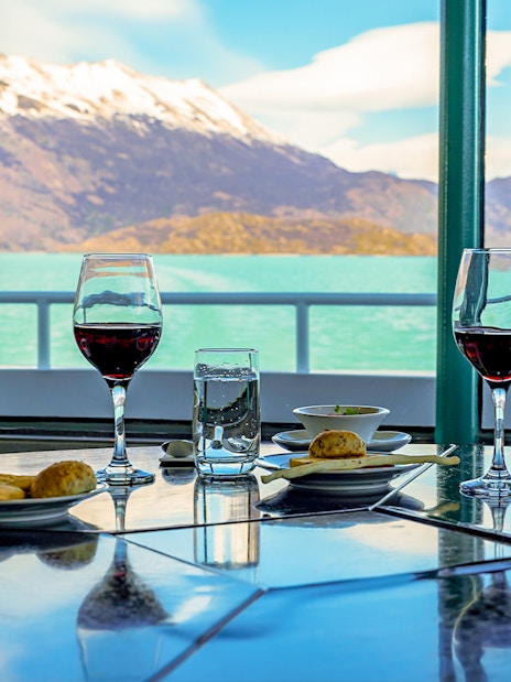 Dining table with wine glasses and snacks on a boat, overlooking Perito Moreno Glacier.