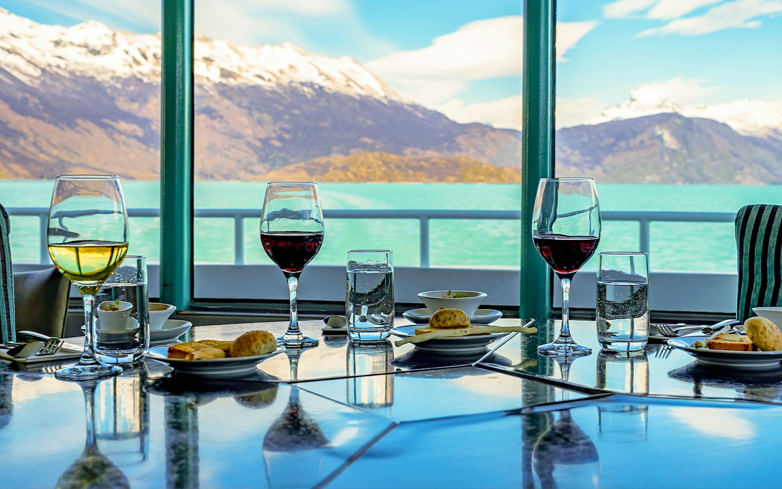 Dining table with wine glasses and snacks on a boat, overlooking Perito Moreno Glacier.