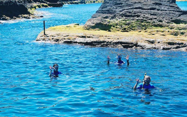Snorkelers in clear blue water near rocky coast on São Miguel Glass Bottom Boat Tour.