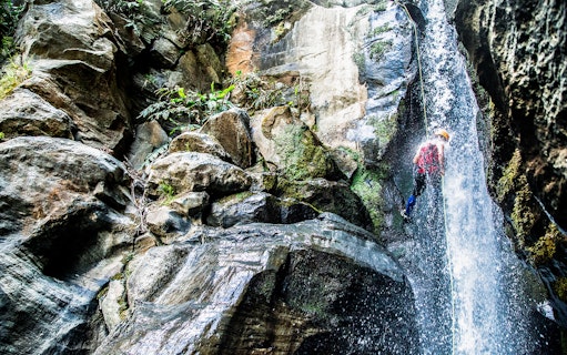 Canyoning down a waterfall at Ribeira dos Caldeirões, surrounded by lush rock formations.