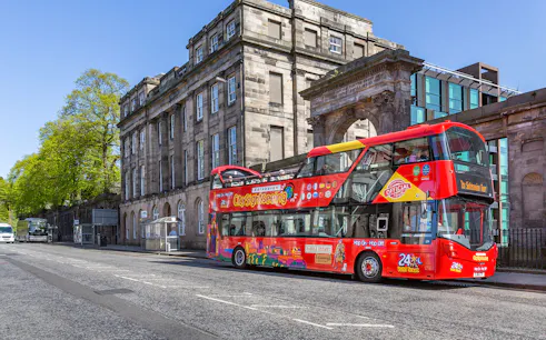 Red double-decker bus on Edinburgh Hop-On Hop-Off Tour near historic stone building.