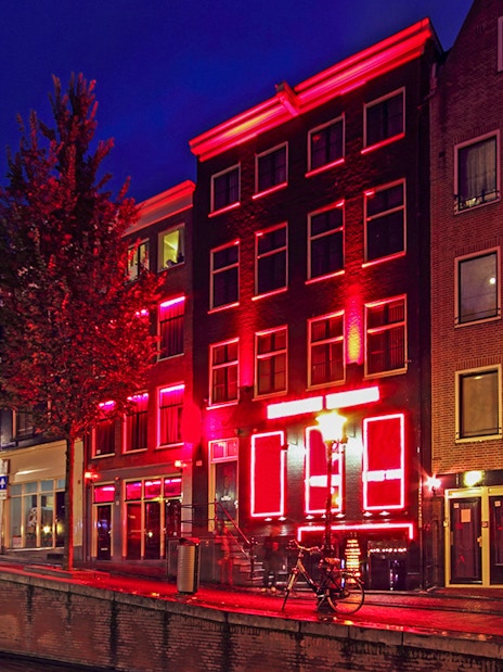 Amsterdam Red Light District buildings illuminated at night along a canal.