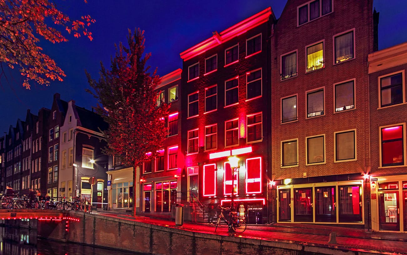 Amsterdam Red Light District buildings illuminated at night along a canal.