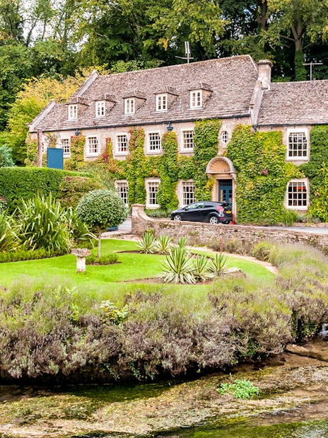 Cotswolds stone house with ivy, garden, and stream on a London day tour.