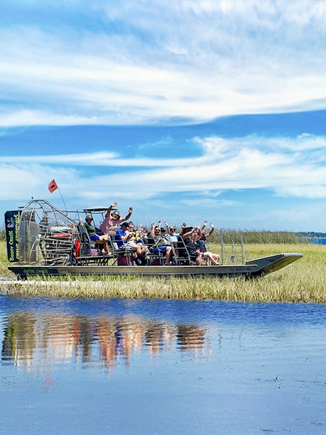 Airboat with tourists on Boggy Creek in Orlando, surrounded by marshland and blue sky.