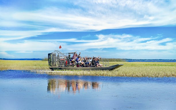Airboat with tourists on Boggy Creek in Orlando, surrounded by marshland and blue sky.