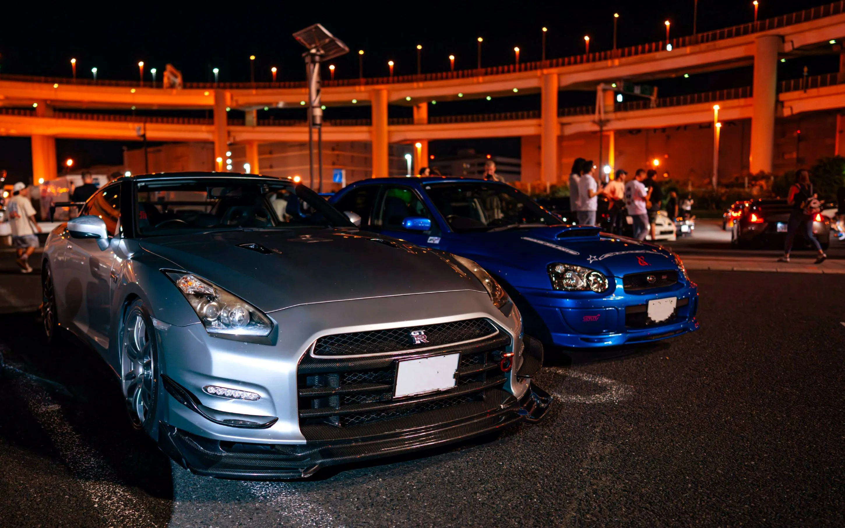 Silver and blue sports cars at a JDM Tokyo car meetup night tour under city lights.