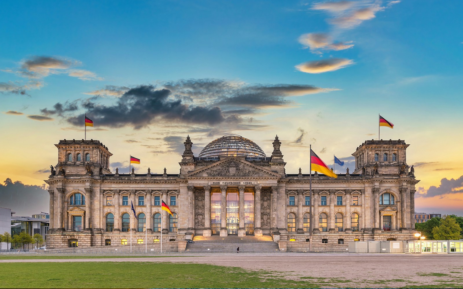 Reichstag Building in Berlin at sunset with German flags flying.
