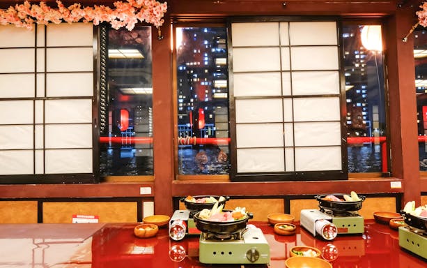 Traditional Japanese dining setup with hot pots on a table, overlooking Tokyo city lights through shoji windows.