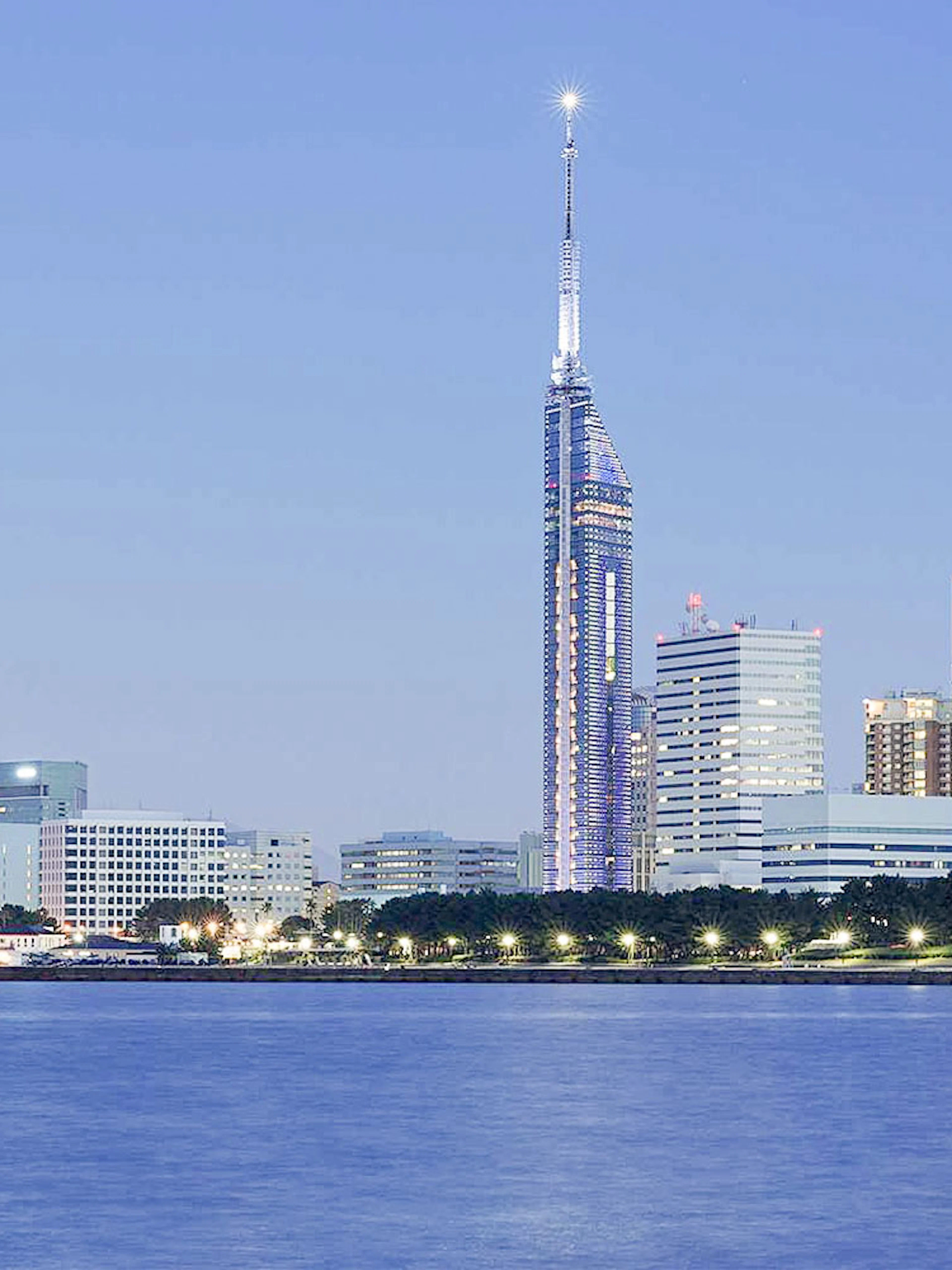 Fukuoka Tower illuminated at dusk with city skyline and waterfront.