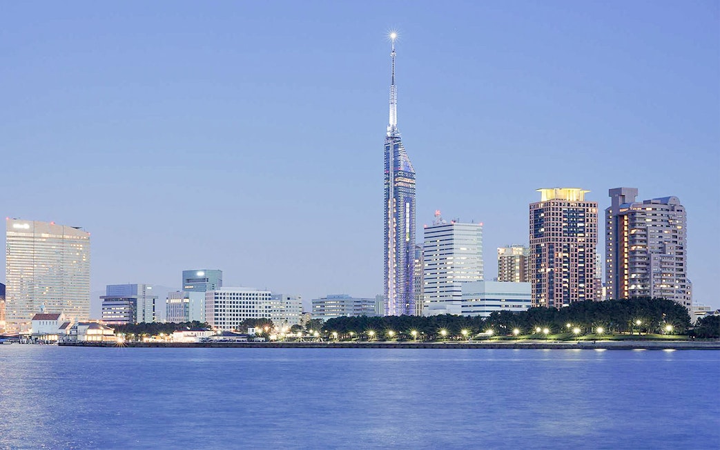 Fukuoka Tower illuminated at dusk with city skyline and waterfront.