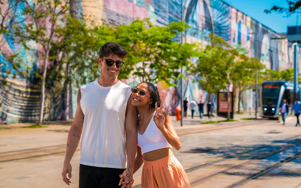 Tourists walking along Olympic Boulevard with colorful mural in the background.
