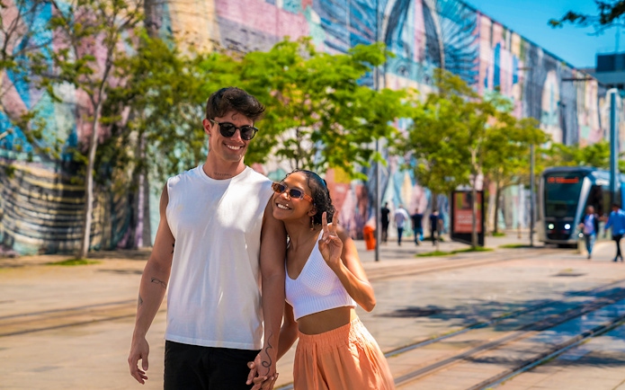 Tourists walking along Olympic Boulevard with colorful mural in the background.