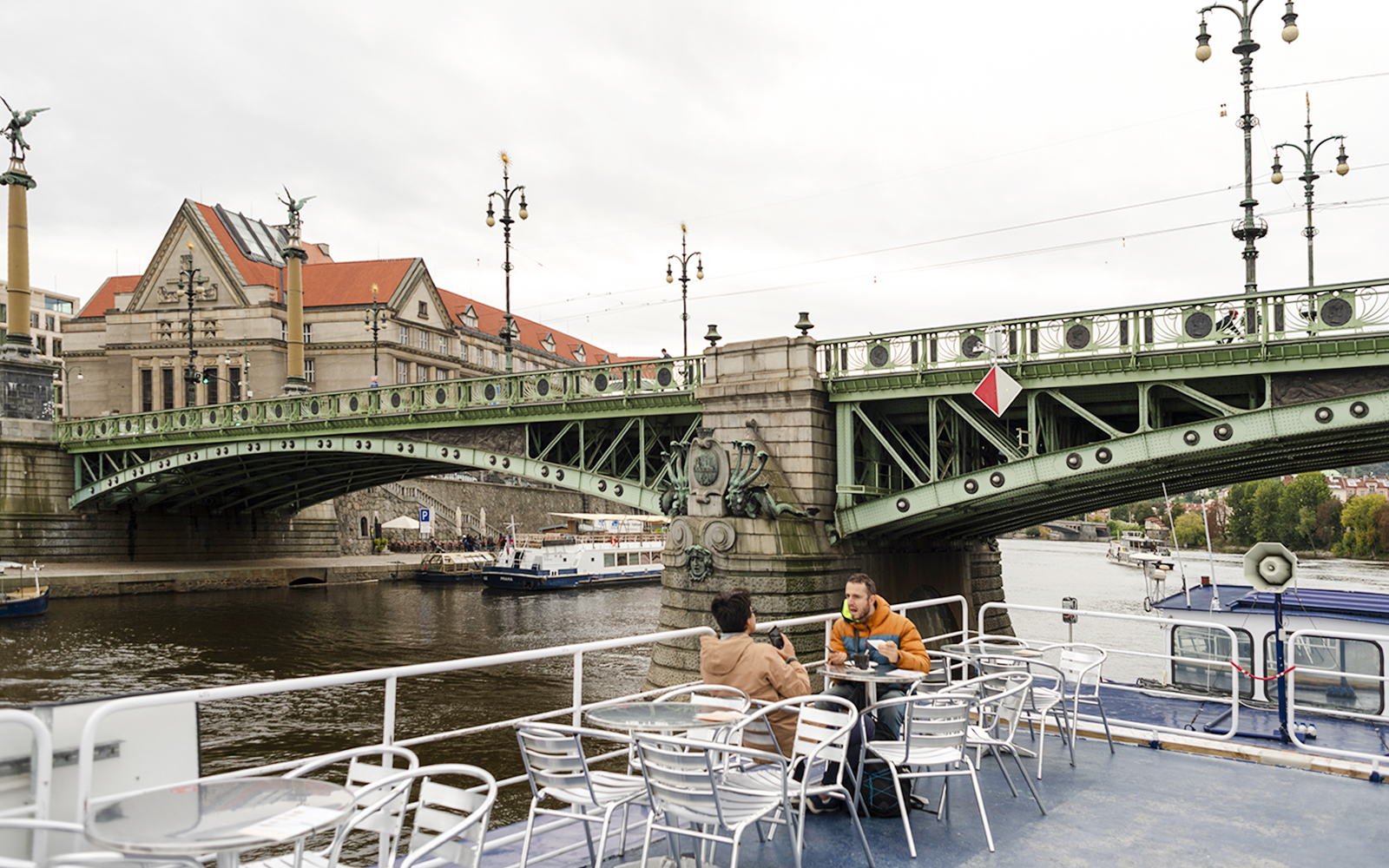 Tourists on a sightseeing cruise in Prague, passing under a historic bridge.
