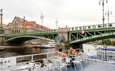 Tourists on a sightseeing cruise in Prague, passing under a historic bridge.