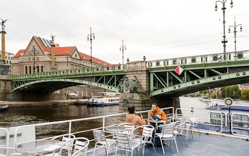 Tourists on a sightseeing cruise in Prague, passing under a historic bridge.