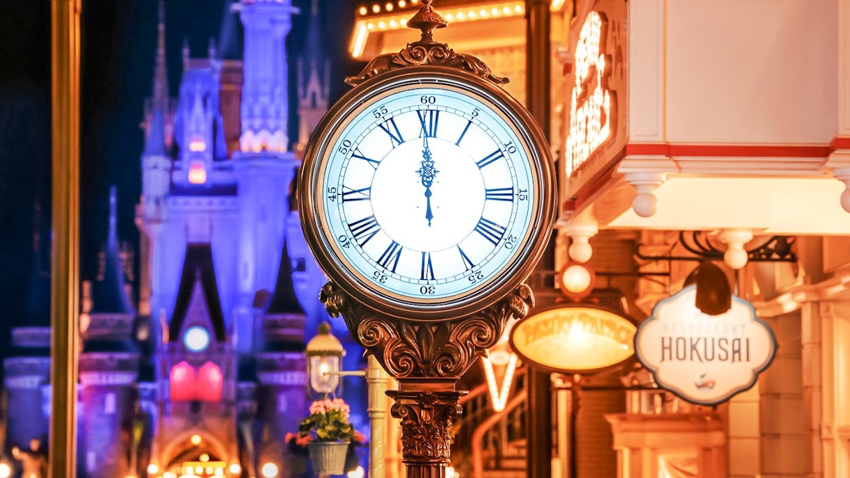 Clock tower in World Bazaar area at Tokyo Disneyland with illuminated castle in background.