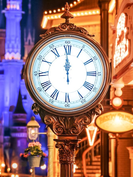 Clock tower in World Bazaar area at Tokyo Disneyland with illuminated castle in background.