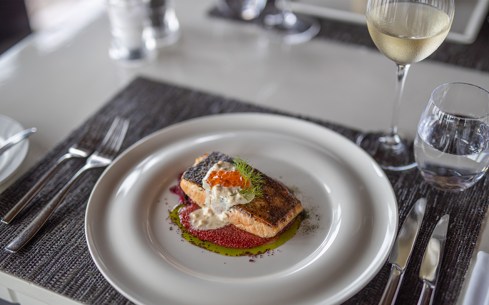 Grilled salmon with sauce and garnish, served with wine, showcasing modern French cuisine.