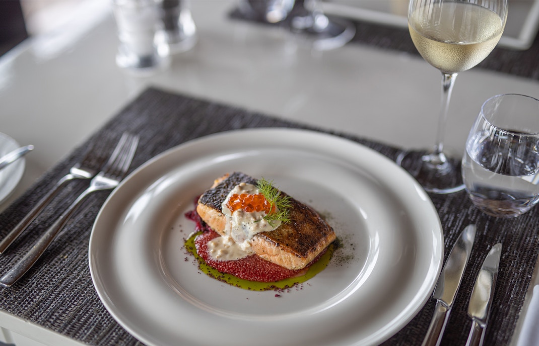 Grilled salmon with sauce and garnish, served with wine, showcasing modern French cuisine.