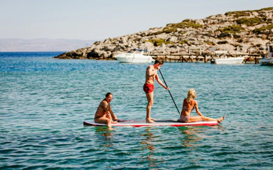 Paddleboarding on Heraklion catamaran cruise with rocky coastline in background.