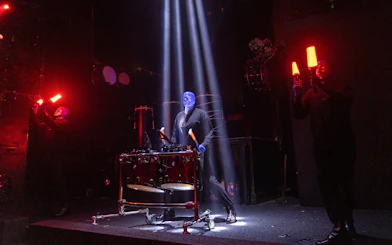 Blue Man Group performing with drums and glowing sticks on stage, Orlando.