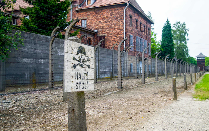 Auschwitz-Birkenau Museum fence and warning sign near Krakow bus tour.